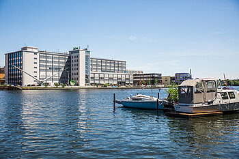 A modern HTW Berlin campus building by the River Spree with boats in the foreground.