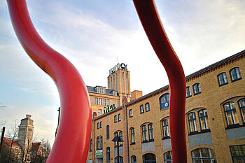 View of an HTW Berlin campus building framed by a striking red sculpture in the foreground.