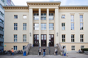 Students walk down the steps in front of a historic university building on the Treskowallee campus.